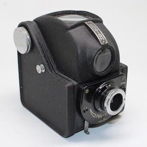 Op de afbeelding: Een zwarte Ensign Ful-Vue boxcamera met een getextureerde afwerking, een zoeker aan de bovenkant, een zilveren opwindknop aan de zijkant en een ronde lens aan de voorkant met de tekst FUL-VUE en 6-oneindig focusmarkeringen.