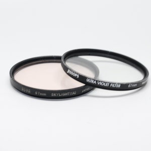 May include: Two 67mm camera lens filters. One is a clear ultra violet filter by Jessops, the other is a pink skylight filter by Hoya.
