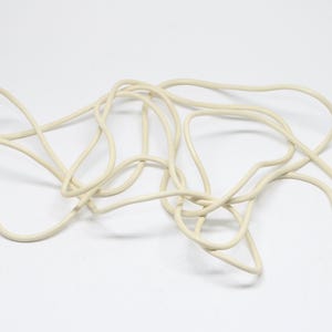 May include: A coiled, off-white cable with two connectors at one end. The cable is made of a flexible material and is lying on a white surface. The connectors have a small, cylindrical shape.