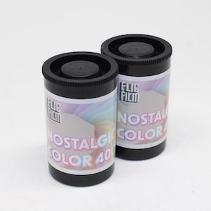 Könnte beinhalten: Zwei zylindrische schwarze Kunststoff-Filmdosen mit Etiketten, die den Text FLIC FILM NOSTALGIC COLOR 400 tragen. Die Etiketten haben einen pastellfarbenen Regenbogenverlauf mit einer geometrischen Form. Die Dosen haben geriffelte schwarze Deckel.