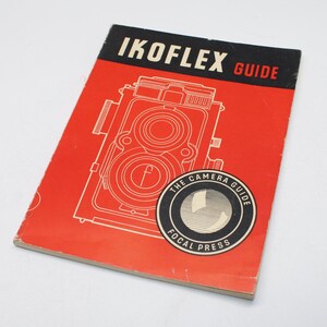 Puede incluir: Un libro guía IKOFLex vintage con una cubierta roja y texto negro. La portada presenta una ilustración detallada de una cámara réflex de doble lente. El libro también tiene un logotipo circular que dice "The Camera Guide Focal Press."