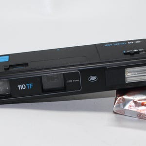 May include: A black 110 TF Teleflash camera with a built-in flash and a lens marked 10/22 44mm. The camera has a blue button and a silver label that says "Boots".