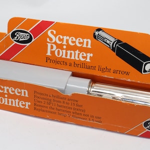 以下が含まれることがあります： 明るいオレンジ色の箱に入った白と銀のスクリーンポインター。箱には「Screen Pointer」と「Projects a brilliant light arrow」の文字が書かれており、Bootsのロゴも入っています。