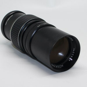 Op de afbeelding: Een zwarte telelens met een zilveren band en de tekst "LENS MADE IN JAPAN" erop gedrukt. De lens is gelabeld met "ACCESS 5268" en "135mm No. 5268".
