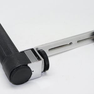 May include: A black and silver camera grip with a textured rubber handle and a rotating knob.