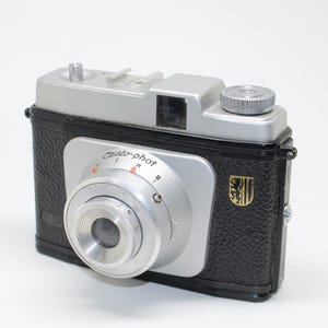 May include: Vintage black and silver Cento-phot camera with a textured body and a silver lens. The camera has a silver top with a viewfinder and a dial. The lens has the text "Cento-phot" on it.
