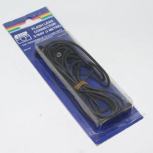 May include: A black flash lead connector, 3-way, packaged in a clear plastic blister pack on a blue and white cardboard backing. The text on the packaging reads "FLASH LEAD CONNECTOR 3-WAY (3 METRE)" and "FOR TRIGGERING UP TO 3 FLASH UNITS".