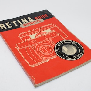Puede incluir: Un libro vintage "Retina Guide" con una cubierta roja y lomo negro. La portada presenta una ilustración de cámara y el texto "Retina Guide" y "Retinette". Un emblema circular dice "The Camera Guide" y "Focal Press".