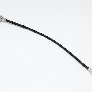 Pode incluir: Cabo de disparo de câmera preto e prateado. O cabo é preto e flexível, com um botão de disparo prateado e uma extremidade roscada para fixação a uma câmera. O cabo tem aproximadamente 30 cm de comprimento.