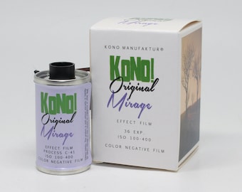 以下が含まれることがあります： 緑と白のラベルが付いた銀色のフィルムケース。ラベルには「KONO! Original Mirage Effect Film Process C-41 ISO 100-400 Color Negative Film」と記載されています。ケースの隣には、同じラベルと「KONO MANUFAKTUR®」という文字が書かれた白い箱があります。