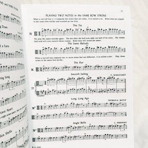 May include: A page from a music instruction book titled Playing Two Notes in the Same Bow Stroke, featuring musical notation for exercises 75 through 79, including The Tie, The Same Melody, The Slur, Smooth Sailing, Long, Long Ago, and Jingle Bells.