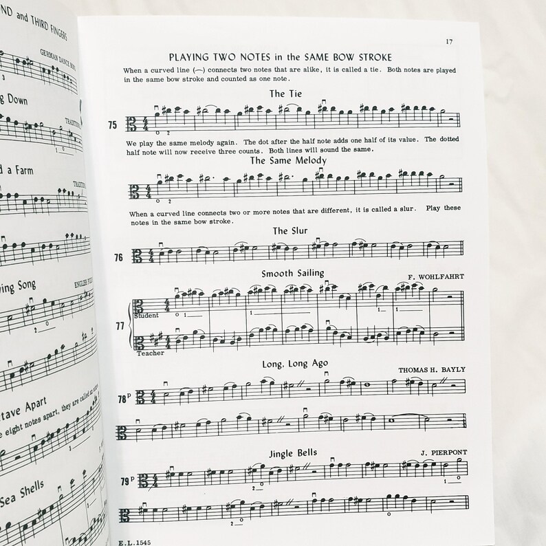 May include: A page from a music instruction book titled Playing Two Notes in the Same Bow Stroke, featuring musical notation for exercises 75 through 79, including The Tie, The Same Melody, The Slur, Smooth Sailing, Long, Long Ago, and Jingle Bells.