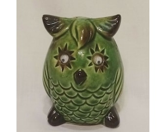 May include: A green ceramic owl figurine with brown eyes and a brown beak. The owl has a textured surface that resembles feathers.