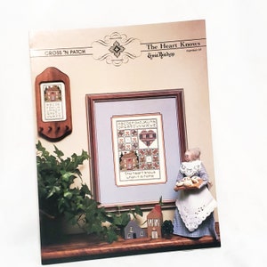 May include: Cross stitch pattern booklet with a colorful illustration of a house, a heart, and the text "The heart knows when it is home". The booklet is titled "The Heart Knows" and is number 40 in a series by Emie Bishop.