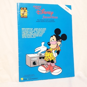 May include: A blue music book titled Easy Disney Favorites for viola, featuring a graphic of Mickey Mouse wearing sunglasses and a floral shirt next to a boombox. The cover includes a list of song titles and a CD included badge at the top left.