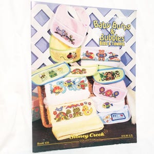 Könnte beinhalten: Ein Kreuzstich-Musterbuch der Stoney Creek Collection mit dem Titel Baby Burps & Bubbles Bibs & Towels, Book 435. Das Cover zeigt verschiedene bestickte Baby-Lätzchen und Handtücher mit bunten Motiven von Tieren, Blumen und Meeresbewohnern.