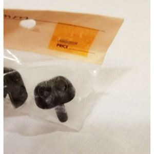 Puede incluir: Dos pies de muebles de plástico negro con forma de hongo y un pequeño tallo. Los pies están empaquetados en una bolsa de plástico transparente con una etiqueta de precio.