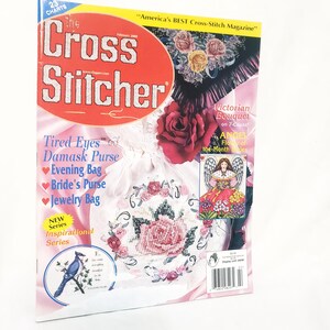 May include: A magazine cover for "The Cross Stitcher" features a red and white logo. The cover showcases cross-stitch patterns, including a rose design, an angel, and a blue bird. Text includes "Victorian Bouquet" and "Evening Bag."