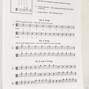 May include: A white sheet of music paper featuring black printed musical notation for the viola. The page includes instructions for bow direction, labeled sections for the D string and A string, and numbered exercises with quarter notes and counts.