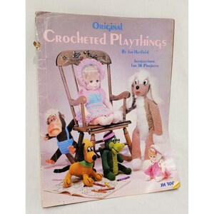 May include: A book cover with the title "Original Crocheted Playthings" by Jan Hatfield. The cover features a crocheted doll sitting in a rocking chair, a crocheted dog, a crocheted monkey, a crocheted alligator, and a crocheted doll. The book includes instructions for 16 projects.