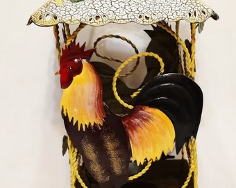 May include: A yellow metal rooster candle holder with a black base and a white roof with sunflowers. The rooster is painted with red, yellow, and brown colors.