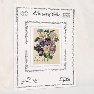 May include: A cross-stitch pattern booklet titled A Bouquet of Violas, a botanical design by Cindy Rice. The cover features a central illustration of purple, yellow, and white viola flowers with green leaves, framed by a decorative black border.