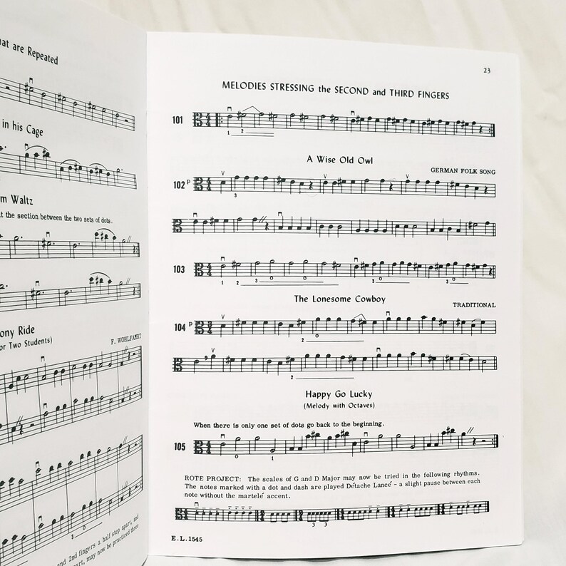 May include: A page from a music instruction book featuring printed musical notation for string instruments. The page includes exercises titled Melodies Stressing the Second and Third Fingers, A Wise Old Owl, The Lonesome Cowboy, and Happy Go Lucky.