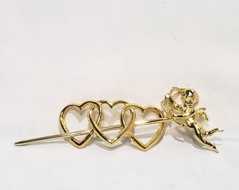 May include: Gold-toned hair stick with three interlocking heart shapes and a small cherub figure holding an arrow.