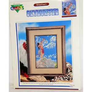 May include: A cross-stitch pattern featuring a Native American man with a bow and arrow, aiming towards the sky. The pattern is titled "Skyhunter" and is by Richard Luce.