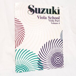 May include: A Suzuki Viola School Volume 4 book. The cover is white with a pattern of teal, purple, and maroon concentric circles. The title "Suzuki" is in black, and "Viola School" and "Viola Part Volume 4" are in purple.