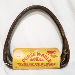May include: A brown "Double Dee" fashion purse handle with a yellow label. The label reads "Purse-N-Able Handle" and "For Macrame, Crochet, Weaving & Fabric Purses". The handle is made of a dark brown material.