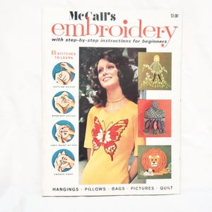 May include: A vintage McCall's embroidery book with step-by-step instructions for beginners. The cover features a woman in a yellow shirt with a butterfly design. The book includes 65 stitches to learn, with examples of outline, straight, lazy daisy, and French knot stitches.