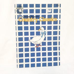 May include: A book titled "Gordon Fraser's Country Classics" with a white duck illustration wearing a blue bow. The cover has a blue and white checkered pattern. The book is a vintage item.