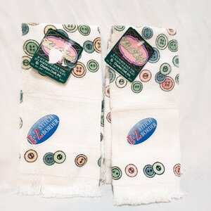 May include: Two white hand towels with a button pattern in pastel colors. Each towel has a fringed edge and a blue oval sticker that reads "E-Z STITCH BORDER." Tags with the text "Charles Craft" are attached.