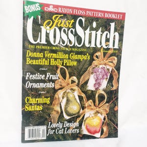 May include: A magazine cover for "Just CrossStitch" featuring cross-stitch fruit ornaments. The cover includes text such as "Festive Fruit Ornaments" and "Lovely Design for Cat Lovers." The magazine is dated December 2000.