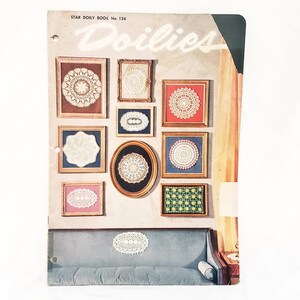 Op de afbeelding: Een pagina uit een vintage "Star Doily Book No. 124" met ingelijste doilies in verschillende vormen en kleuren. De doilies worden tentoongesteld aan een muur boven een blauwe bank. Het woord "Doilies" staat bovenaan de pagina.