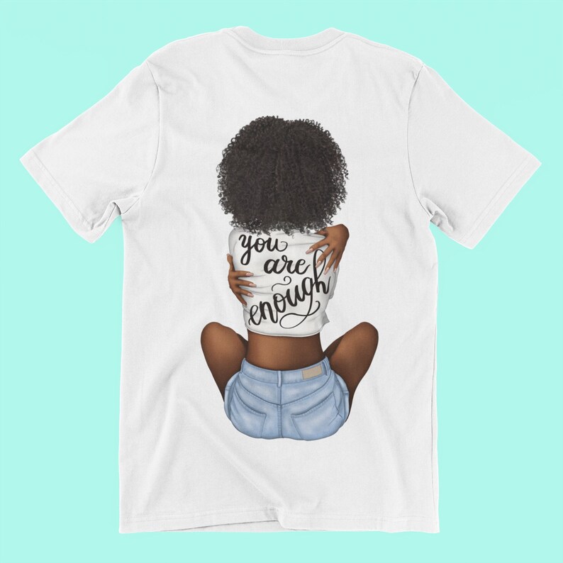Pu&ograve; includere: T-shirt bianca con una grafica di una persona che si abbraccia, con le parole "you are enough" in corsivo nero. La persona indossa pantaloncini di jeans e ha i capelli ricci scuri.