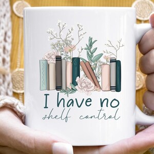 May include: White ceramic mug with a floral design and a stack of books. The text "I have no shelf control" is printed on the mug.