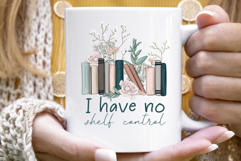 May include: White ceramic mug with a floral design and a stack of books. The text "I have no shelf control" is printed on the mug.