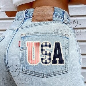 May include: Light blue denim jeans with a back pocket featuring a patriotic "USA" patch. The patch includes red and white stripes, a blue and white gingham pattern, and a navy blue polka dot design.