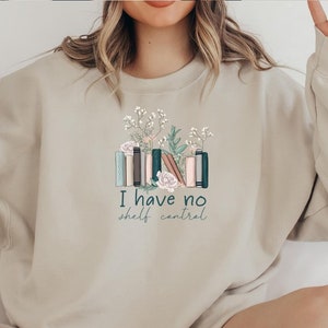 May include: A beige sweatshirt with a graphic of a stack of books with flowers and the text "I have no shelf control".
