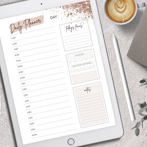 May include: A digital daily planner displayed on a tablet. The planner features sections for time slots, today's focus, mood, water intake, and notes. The design includes a neutral color palette with decorative accents and text that reads "Daily Planner".