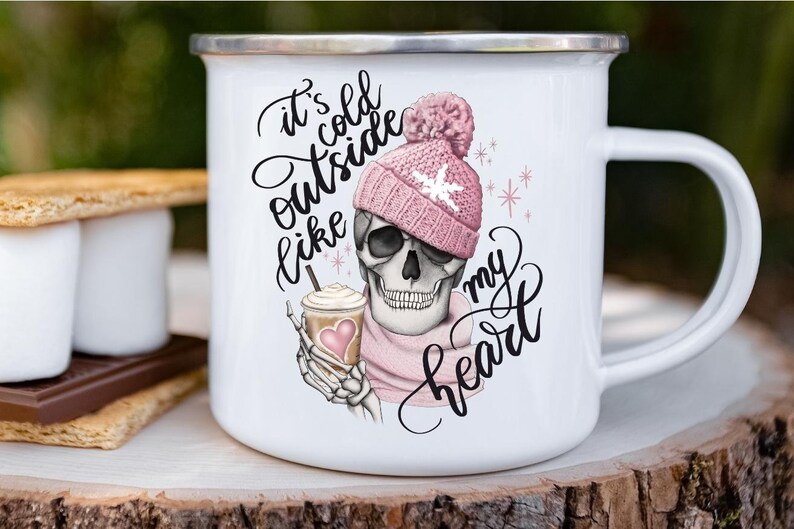 May include: White enamel mug with a silver rim featuring a skull wearing a pink knit hat and scarf. The skull is holding a coffee cup with a heart. Text on the mug reads "It's cold outside like my heart."