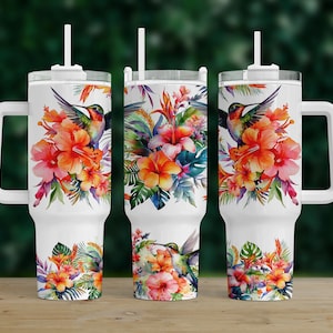 May include: White stainless steel tumbler with a handle and a lid. The tumbler features a colorful watercolor design of tropical flowers and hummingbirds.