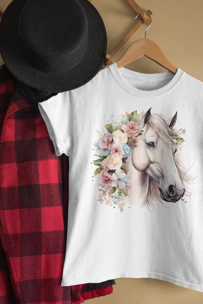 May include: White t-shirt with a watercolor illustration of a white horse with a floral crown. The flowers are pink, blue, and white.