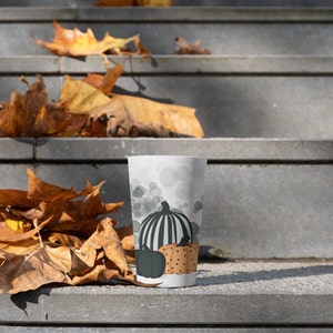 Puede incluir: Un vaso blanco con un dise&ntilde;o de calabaza oto&ntilde;al. El vaso tiene una calabaza a rayas blancas y negras, una calabaza verde oscuro y una calabaza con lunares naranjas. El fondo tiene c&iacute;rculos grises.