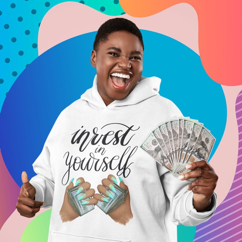 May include: White hoodie with the text "invest in yourself" in black cursive lettering. A pair of hands holding stacks of money with green nail polish are shown below the text.