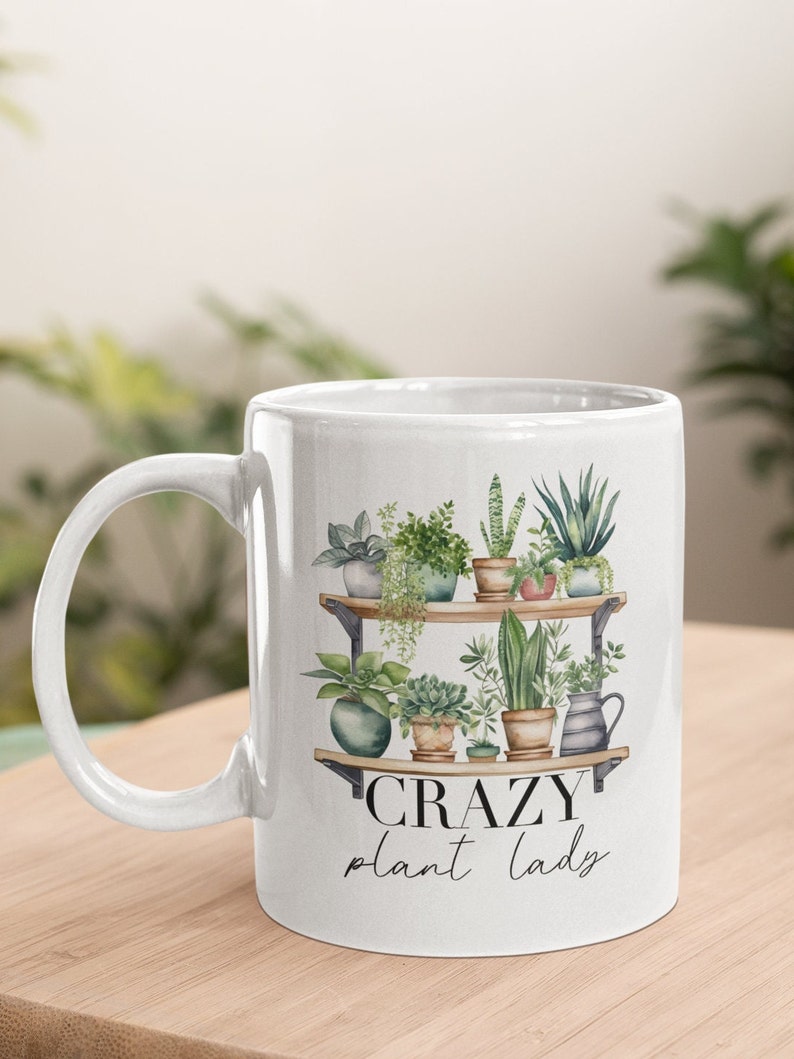 May include: White ceramic mug with a black and white graphic of a shelf with potted plants and the text "CRAZY plant lady".