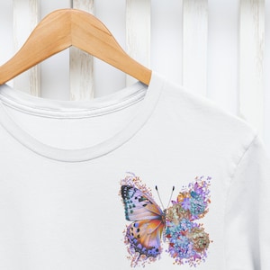 Puede incluir: Camiseta blanca con un gr&aacute;fico de mariposa colorido. La mariposa est&aacute; hecha de flores y tiene acentos morados, naranjas y verdes.