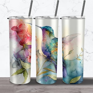 Puede incluir: Tres vasos de acero inoxidable con diferentes diseños de acuarela. El primer vaso presenta un diseño floral con tonos rosados, morados y verdes. El segundo vaso presenta un colibrí con tonos azules, verdes y morados. El tercer vaso presenta un colibrí con tonos azules, verdes y amarillos.